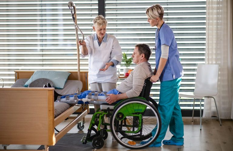Pflegekräfte betreuen einen Patienten im Rollstuhl – Symbol für Pflegevorsorge